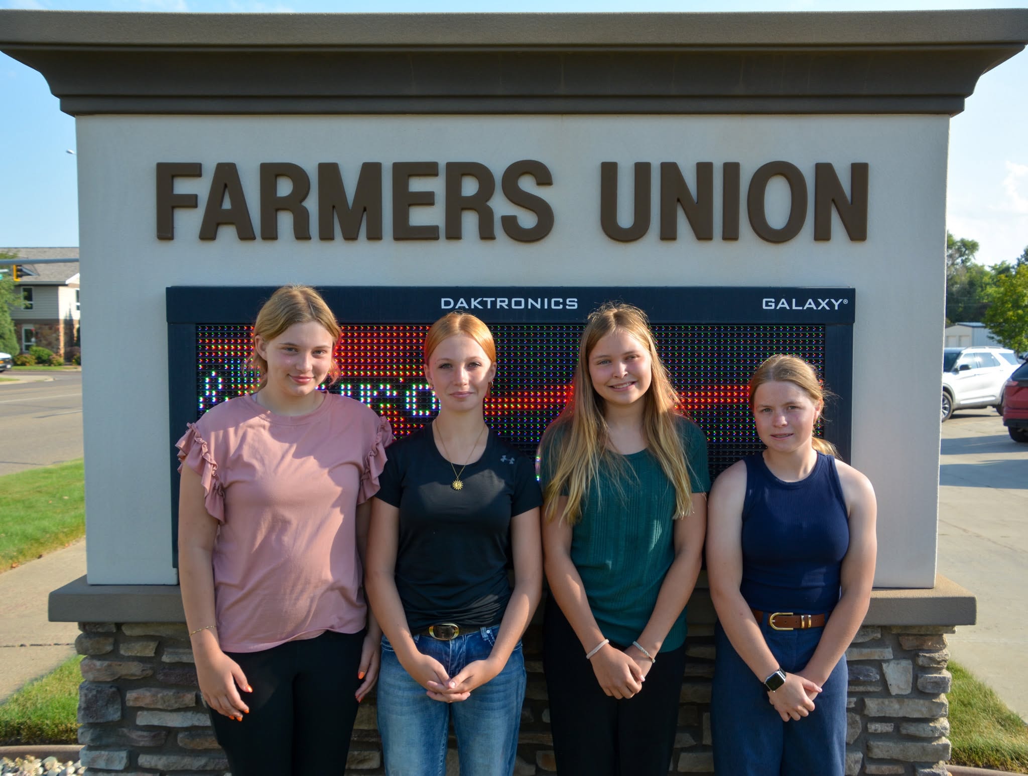 Four young women in front of the Farmers Union sign